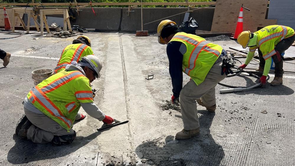 Construction workers smooth out concrete at a bridge expansion joint.