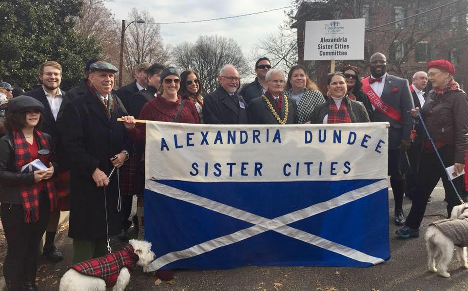 Group of people standing behind flag that says Alexandria Dundee Sister Cities