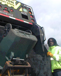 Photo of person standing beside a trash truck as a residential trash cart is emptied