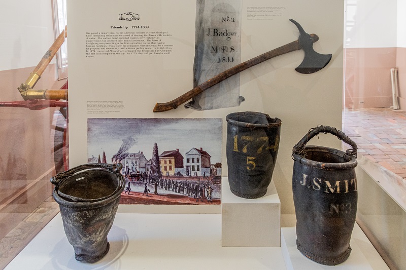 Exhibit case at Friendship Firehouse with hatchet and fire buckets