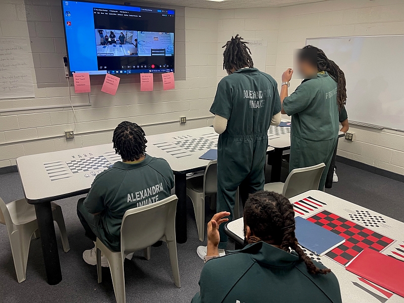 four men in jail jumpsuits in a classroom