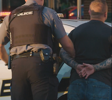 A man with his hands behind his back is led away by an officer