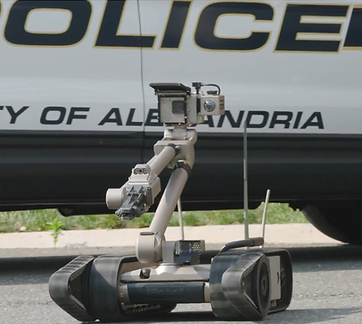 A wheeled robot with a camera on an extendable arm in front of a police cruiser