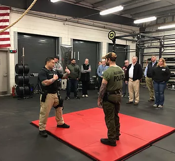 Two men face each other on a red padded mat in a room outfitted with equipment designed for physical training