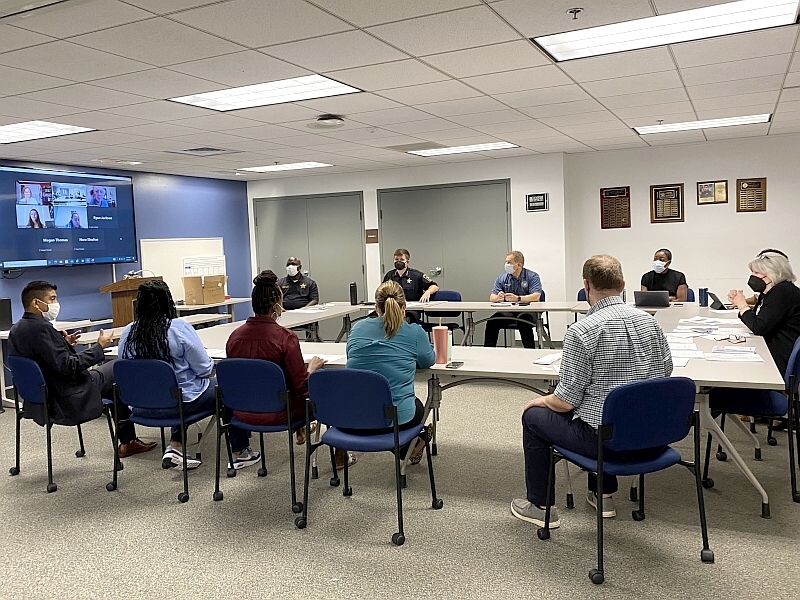 several people including deputies in uniform in a meeting with others appearing on a video screen