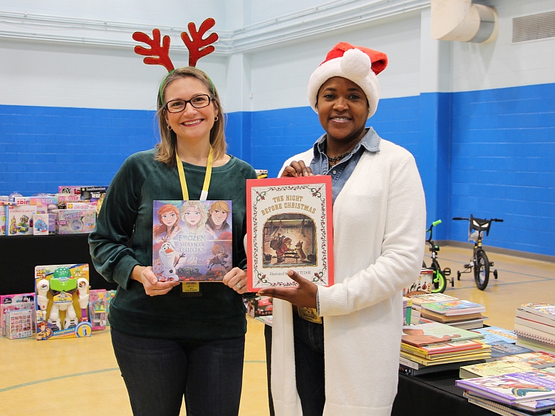 two civilian employees wearing holiday hats and holding children's books