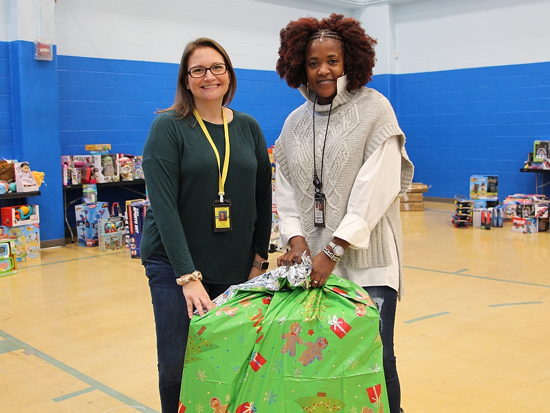 two civilian employees holding a large bag with holiday markings