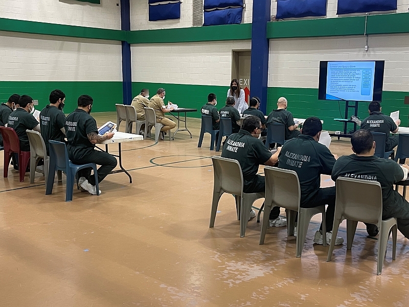 several inmates in jumpsuits listening to an instructor