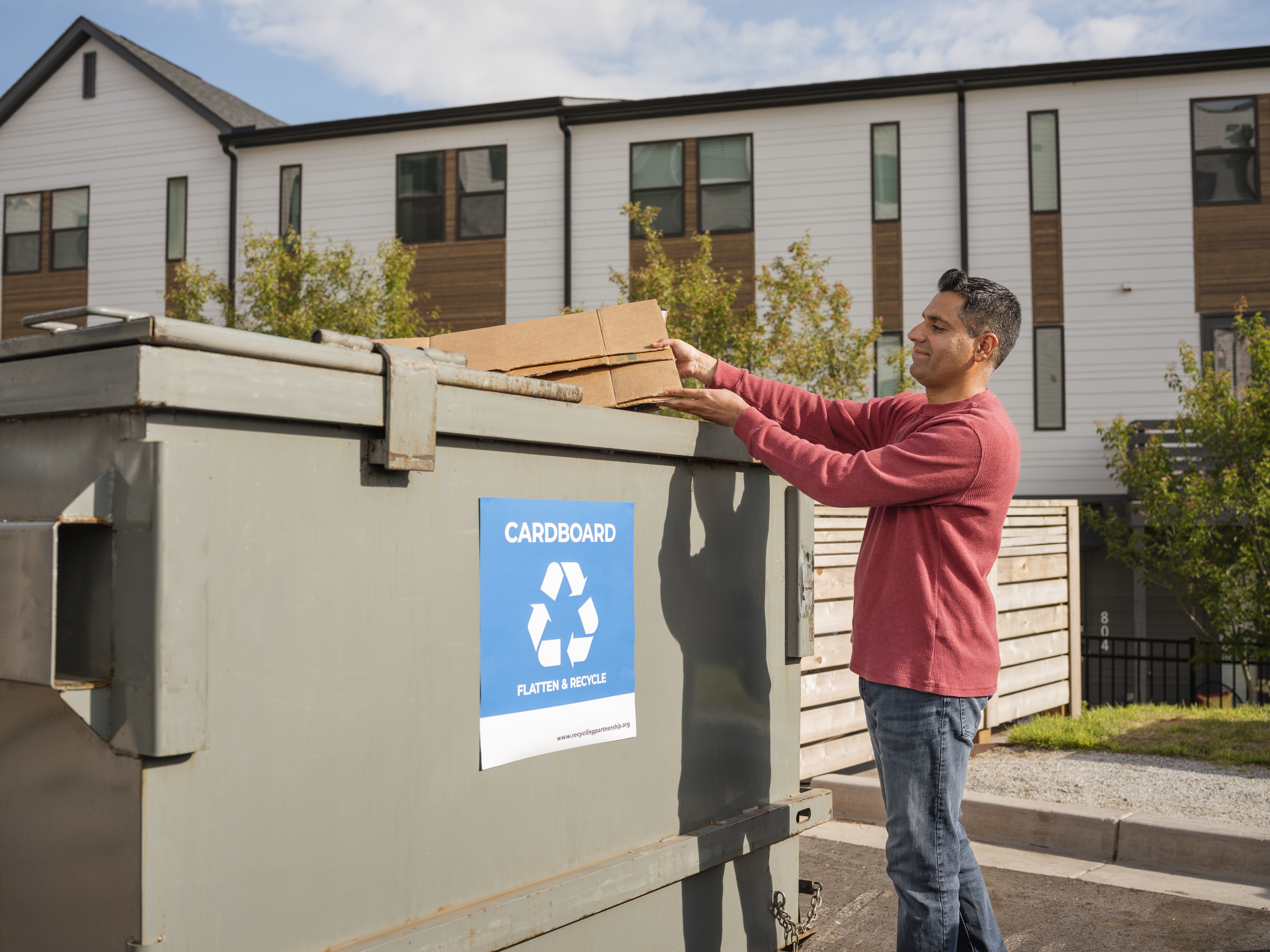 Man recycling flattened cardboard at apartment recycling dumpster