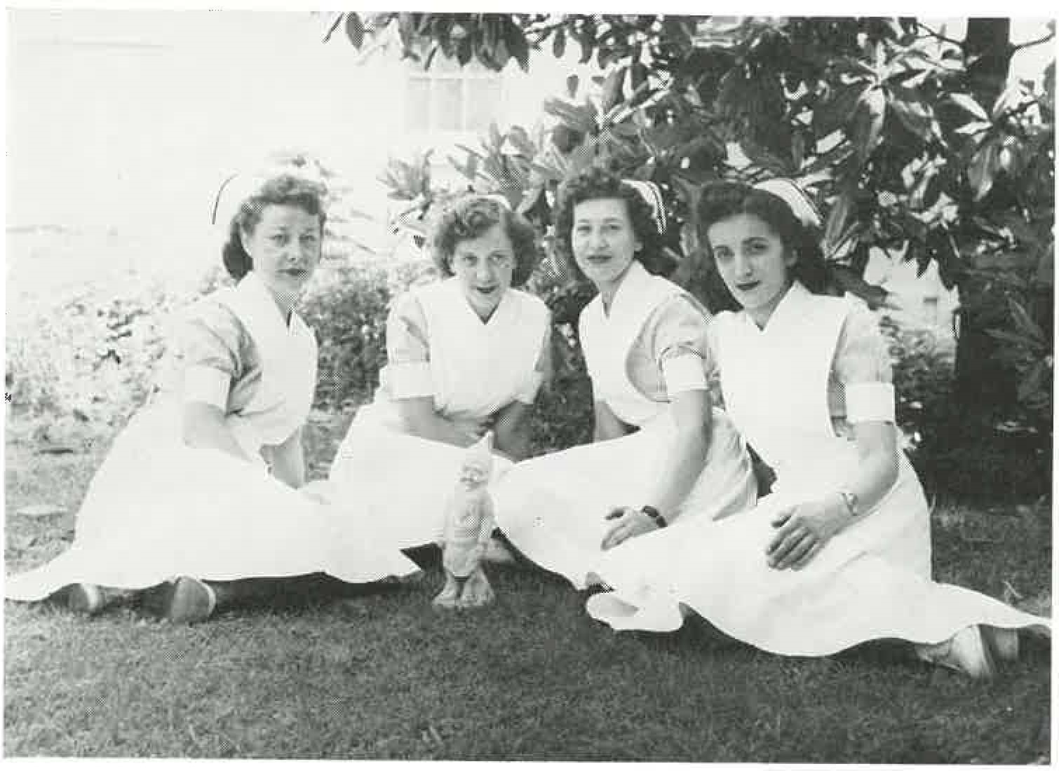 Four women in nursing uniforms, sitting on grass