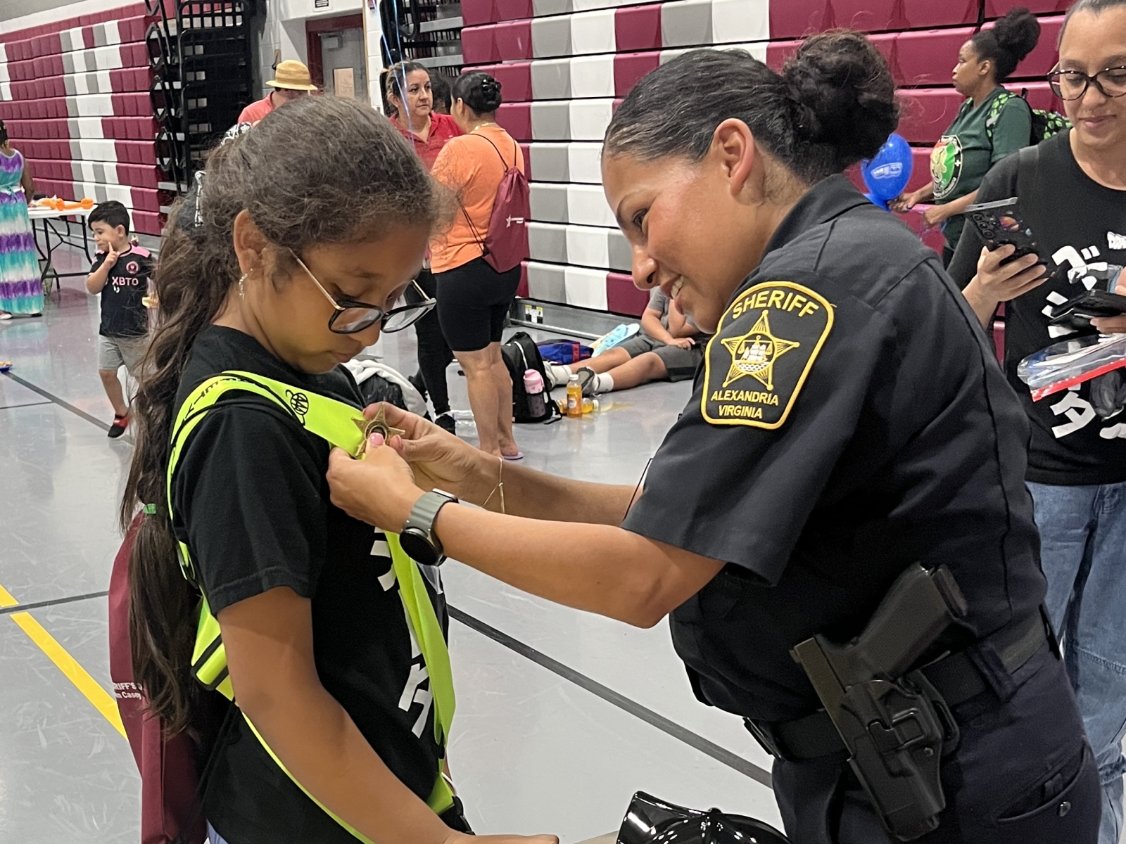 Sheriff's deputy in a blue uniform pins a star on the bright yellow belt of a student safety patrol member