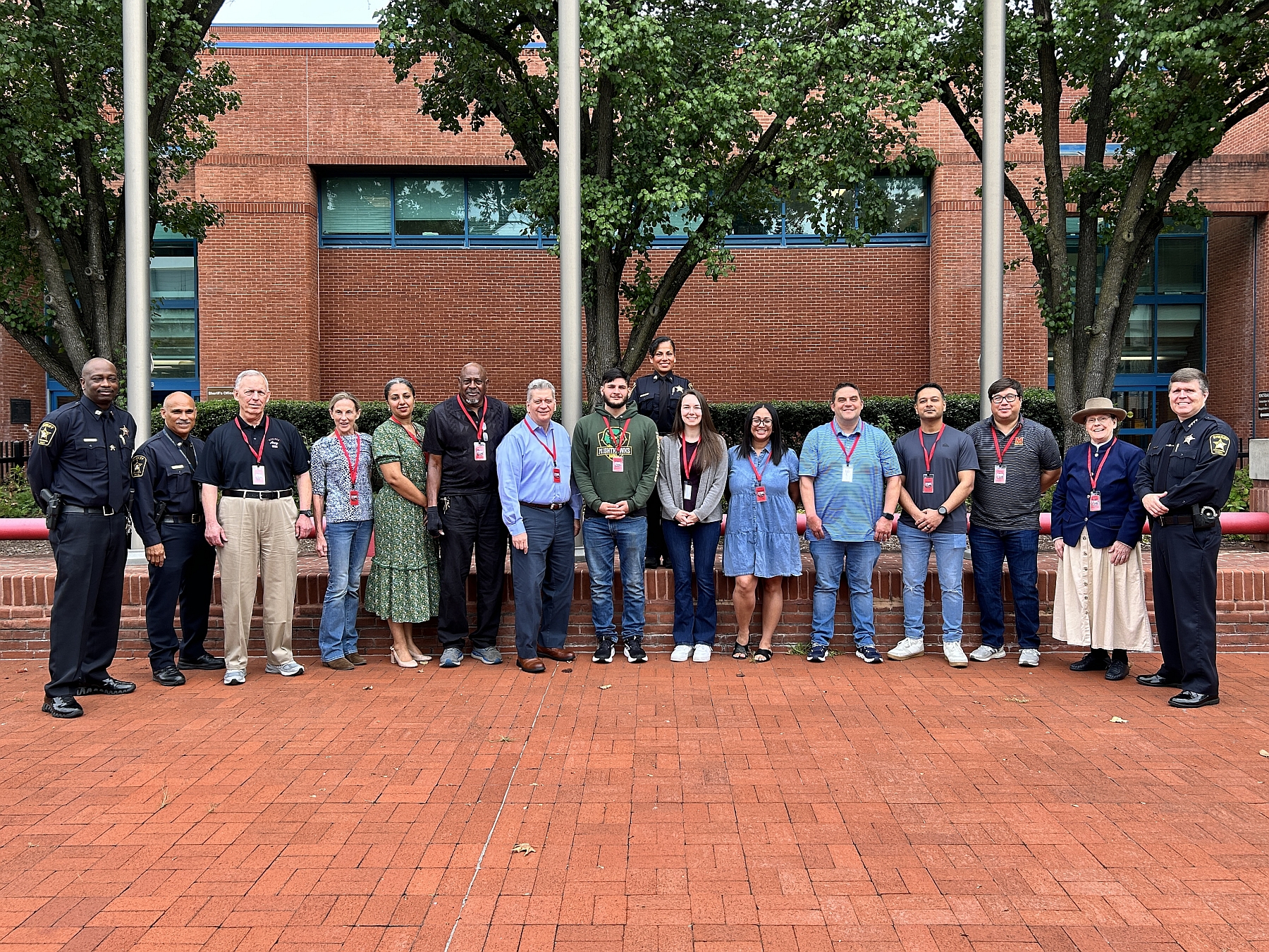 Sheriff and three deputies, all in blue uniforms, standing in a line with 12 civilians outside the Sheriff's Office