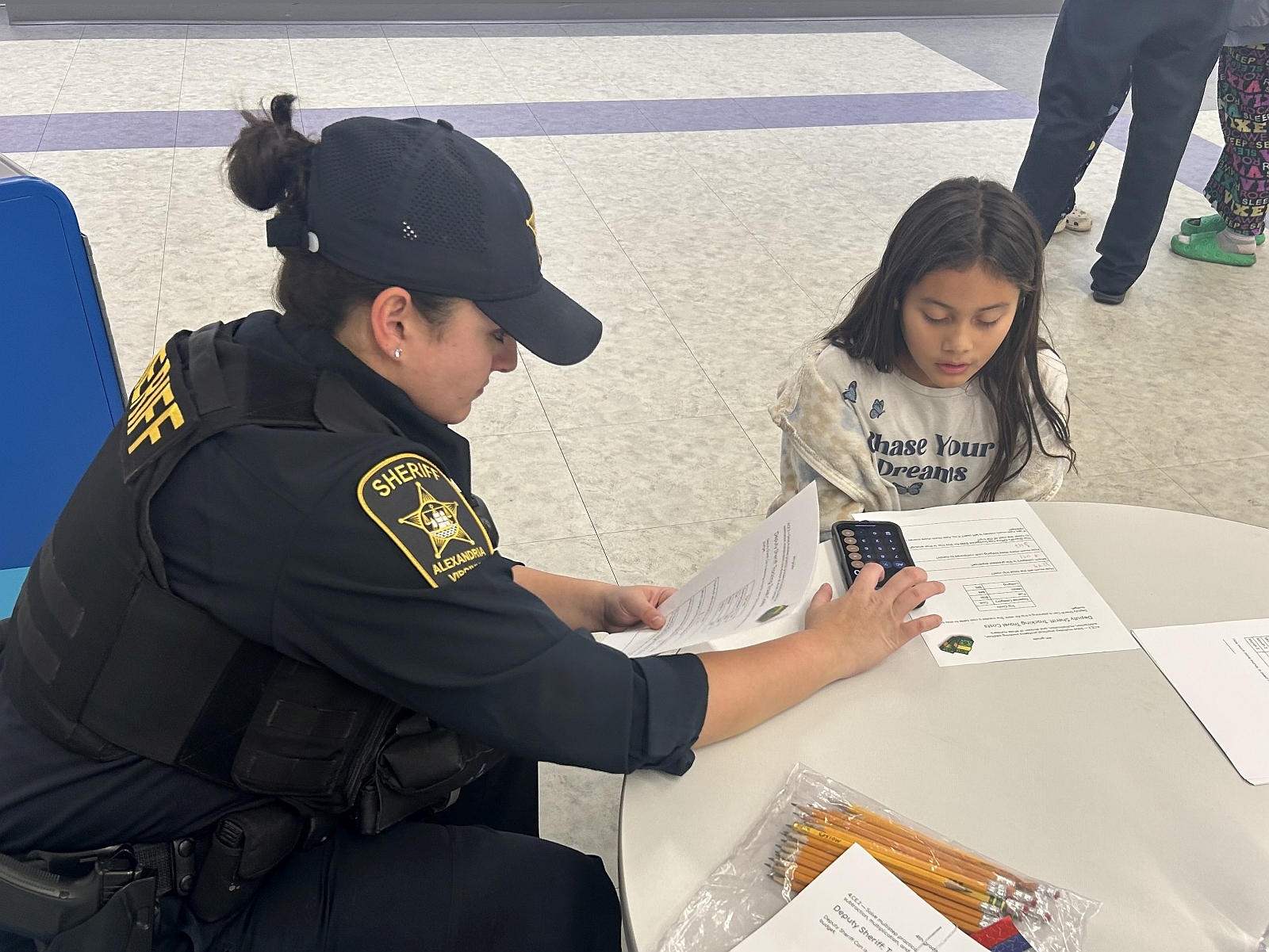 Deputy wearing a blue uniform helps an elementary school student with math worksheets and a calculator
