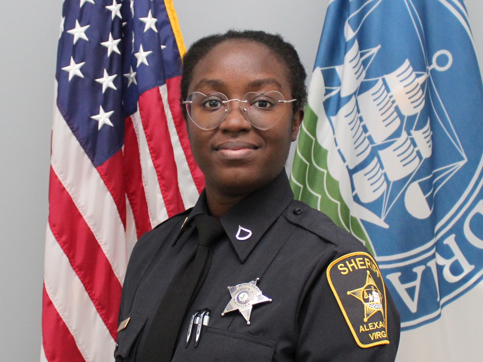 Official portrait of Deputy Haines wearing blue uniform with U.S. and Alexandria flags in background