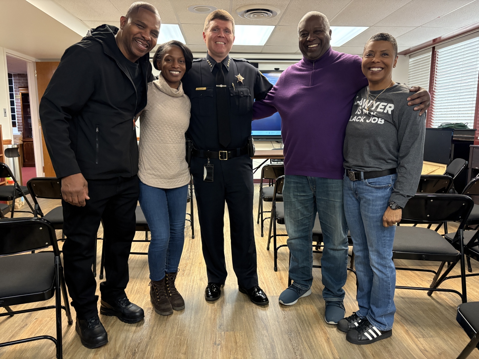 Five people standing close together, with four in casual civilian clothing and the center wearing a blue Sheriff's uniform
