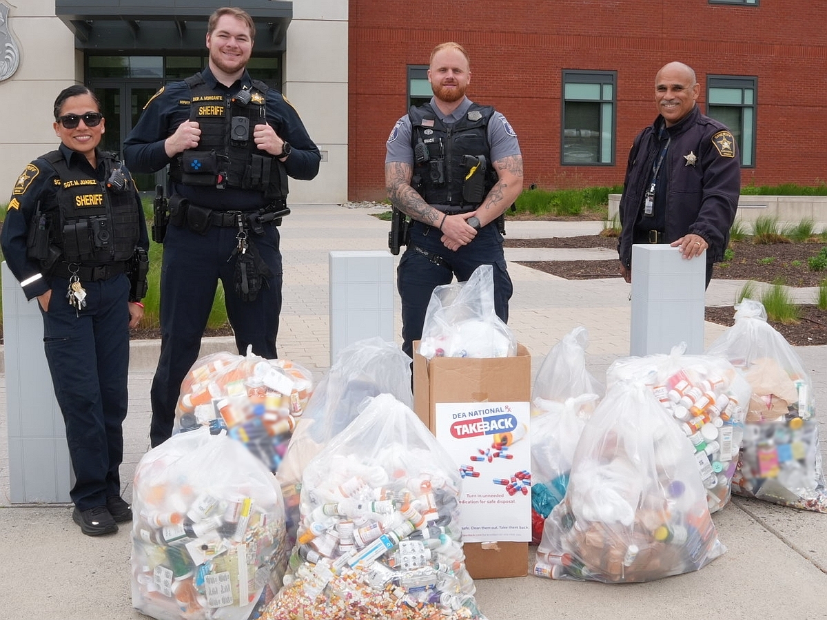Three deputies and one police officer standing with several large clear plastic bags and a Drug Take Back box in front of them