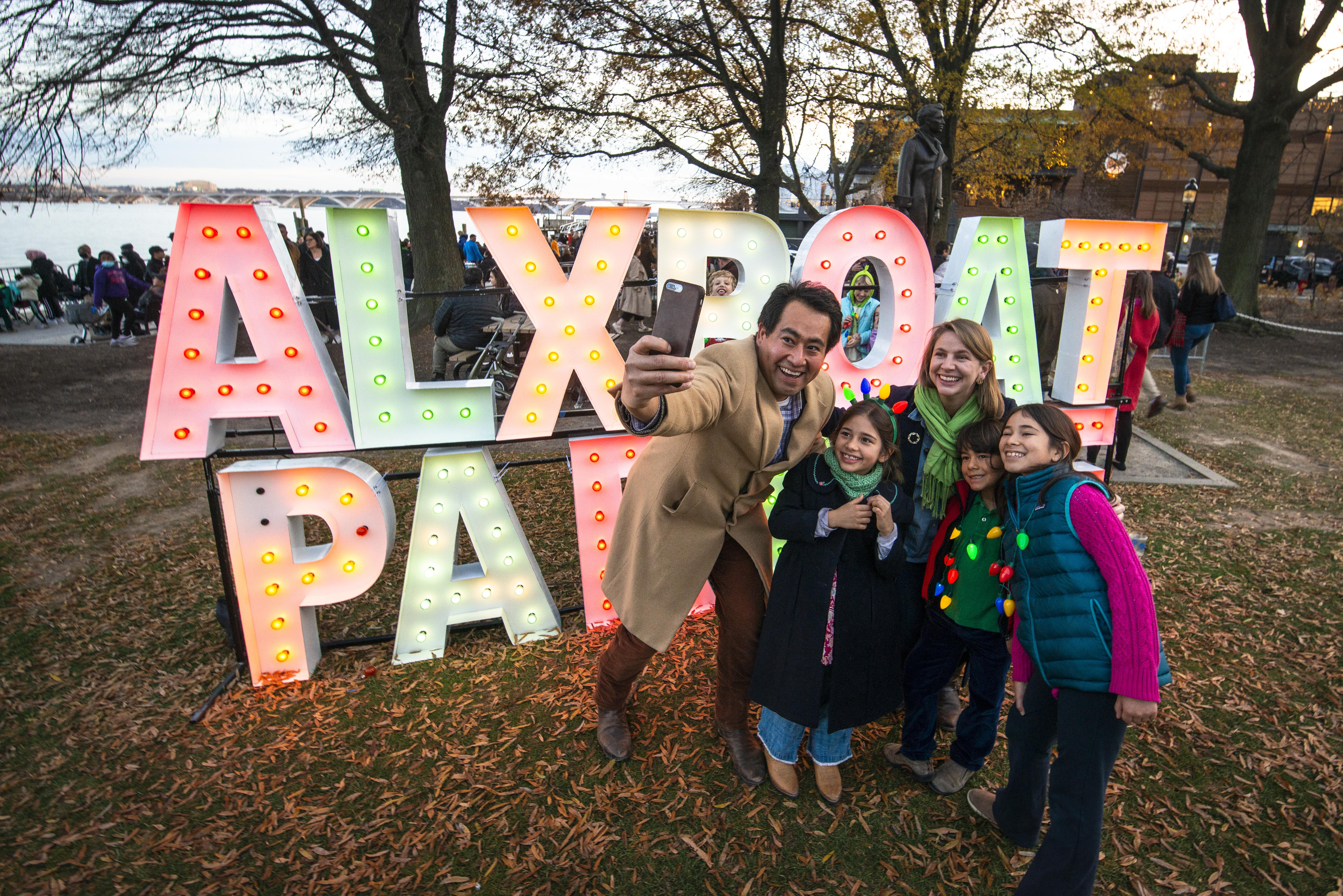 A family poses in front of a light-up sign at the Alexandria Boat Parade