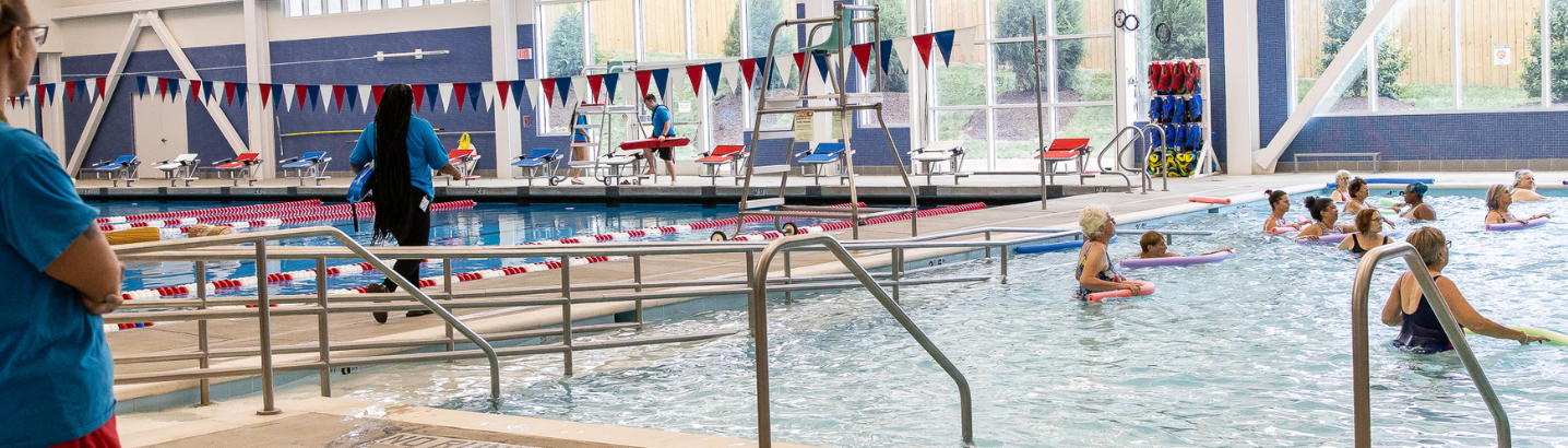 Minnie Howard Aquatics Facility with lifeguards on the left watching patrons and community members on the right partaking in a swim lesson