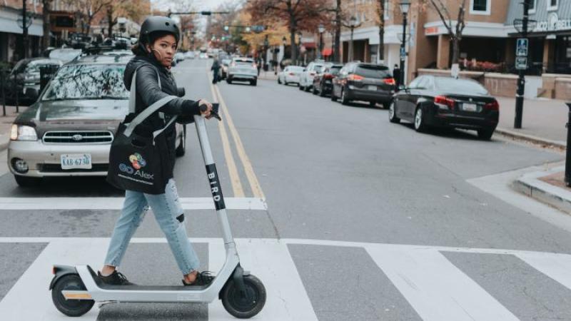 Photo of a person walking a Bird scooter across King Street, in crosswalk