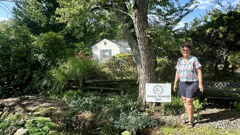 woman standing in yard with award winner 2023 sign