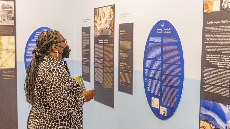 Women in printed dress looking at information posted on a blue wall. 