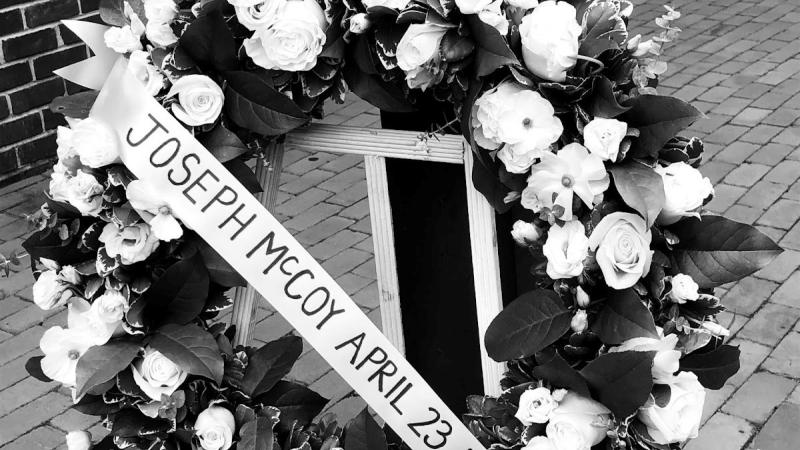 Image of a wreath with a ribbon with the words Joseph McCoy, April 23, 1897 written across it.