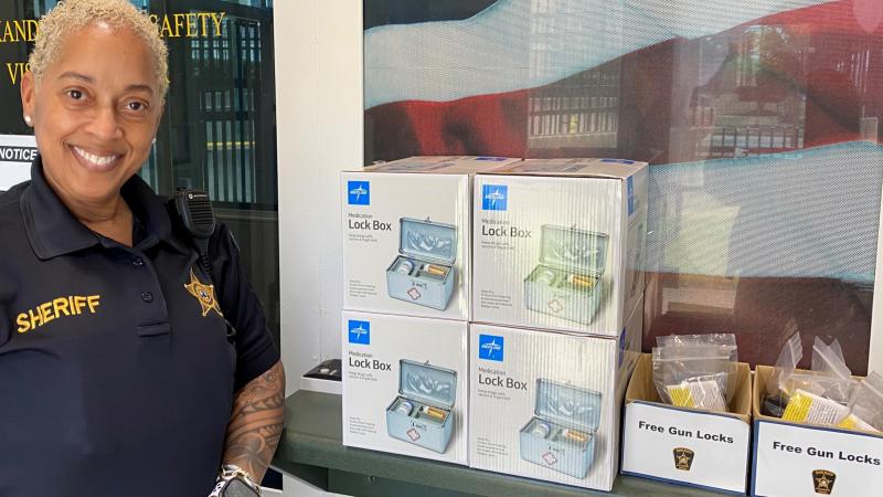 deputy standing next to display of small lock boxes in cartons and smaller boxes with labels reading Free Gun Locks