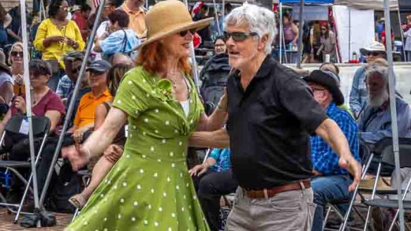 A woman wearing a 1940s-esque dress and man swing dancing outside the D-Day stage. 
