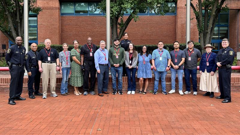 Sheriff and three deputies, all in blue uniforms, standing in a line with 12 civilians outside the Sheriff's Office