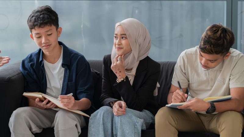 Three teens learning and writing in notebooks sitting on a couch