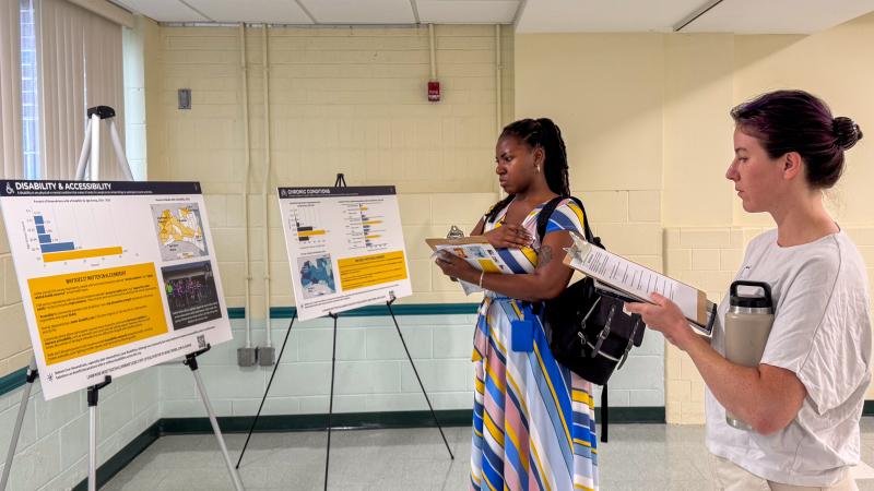 Two adults with clipboards look at a poster with health statistics