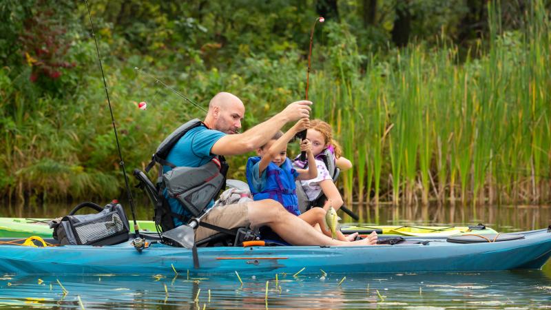 Image of a father and two kids in a kayak while holding fishing poles