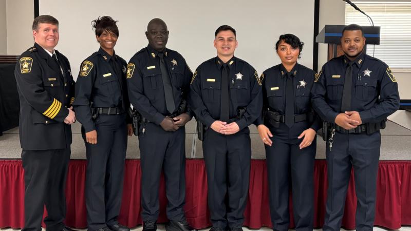 Sheriff in formal uniform standing next to five recruit deputies in blue uniforms at their graduation