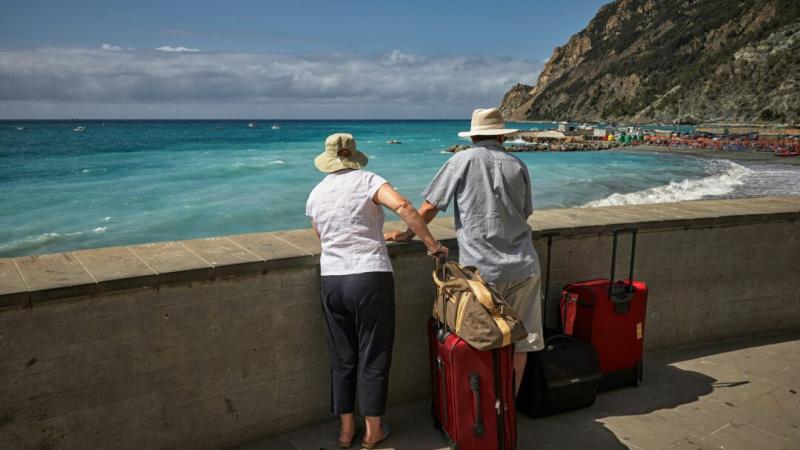 two seniors with suitcases looking out on a scenic body of water