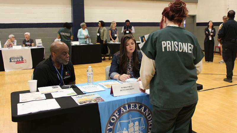 Inmate in green uniform that says Prisoner on the back speaking with two members of the Workforce Development team at the Reentry Resource Fair