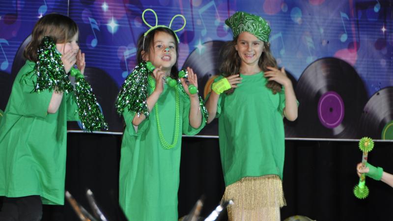 Three young girls on the stage dressed in green clothing and accessories