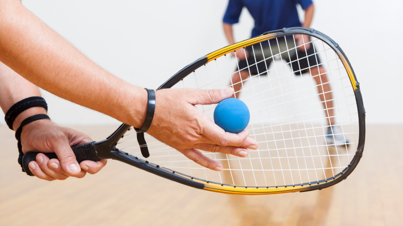 Hand holding a racquetball racquet and another hand holding a blue ball