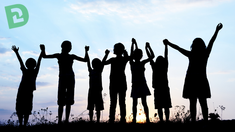 Silhouette of children holding hands while they raise their hands up in the air. Setting is outside with a blue and purple sky and the sun rising