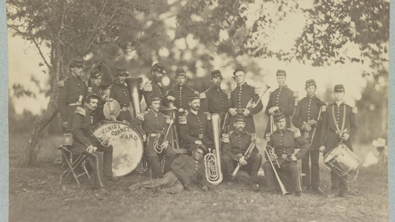 Fifteen musicians pose with their instruments in this black-and-white photograph. The drum is labeled “Emira Cornet Band.”
