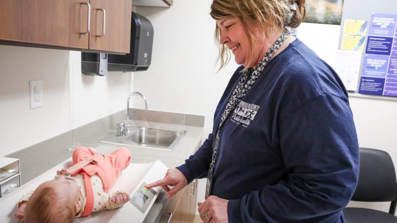 Health department employee measures a baby's weight. The baby is lying on a scale.