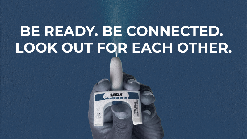 An informational graphic with a textured dark blue background featuring large, white, all-caps text at the top that reads: "BE READY. BE CONNECTED. LOOK OUT FOR EACH OTHER." Centered below the text, a hand rendered in a stylized, monochromatic grey tone holds a white Narcan nasal spray device. The device is being deployed, showing a fine white mist spraying upward from the nozzle toward the text.