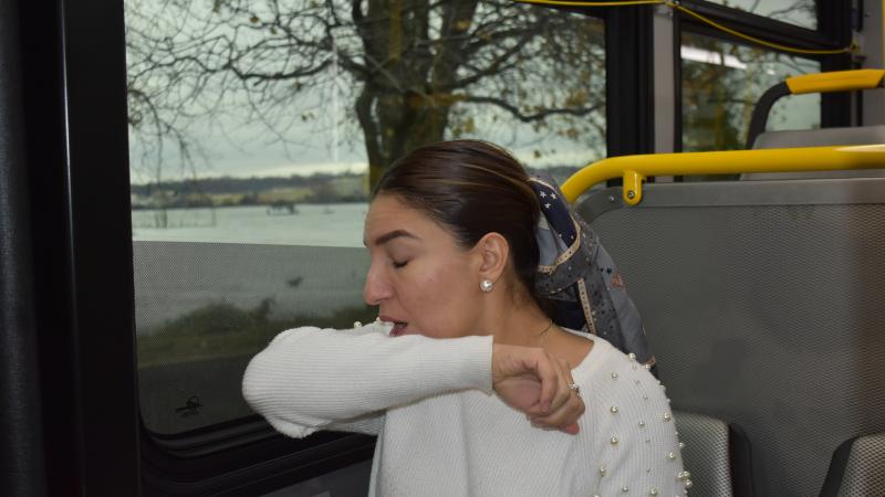 woman sneezing into her elbow on a bus