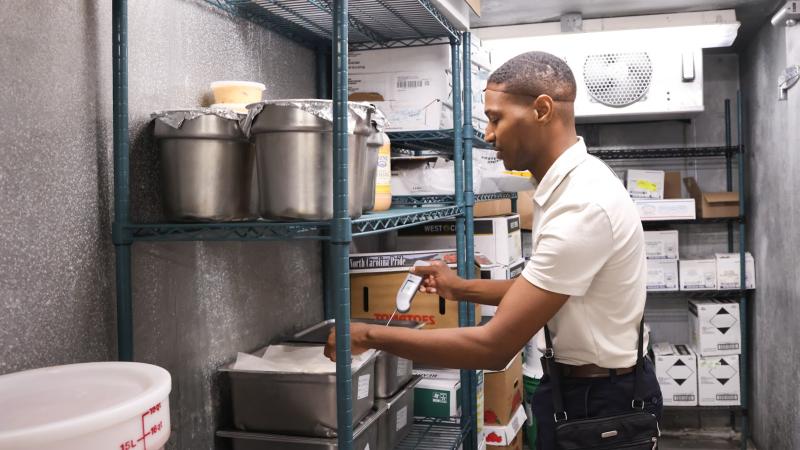 In a commercial kitchen, a man uses a thermometer to measure food temperatures