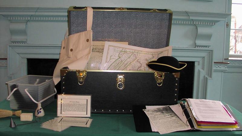 The outreach kit is displayed to show it contains 18th century objects like a haversack and tricorn hat, historic maps, and a teacher resource notebook. 