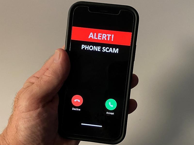 close up of a hand holding a cell phone with a display reading Alert Phone Scam