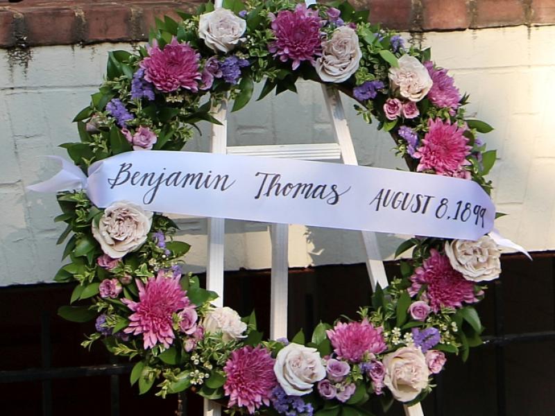 a memorial wreath with pink, white and purple flowers and a banner reading: Benjamin Thomas August 8, 1899