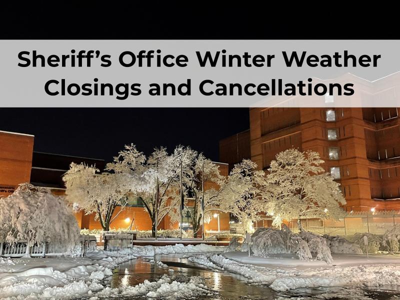 snow covered trees and ground with jail in background at night and message: Sheriff's Office Winter Weather Closings and Cancellations