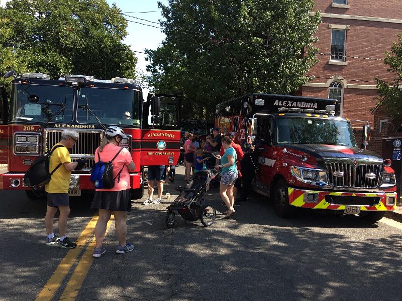 Adults and children stand near a parked Alexandria fire truck and ambulance.