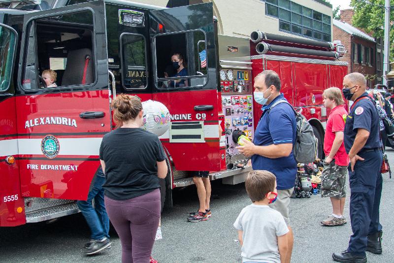 Adults and children stand in line to sit in a fire truck.
