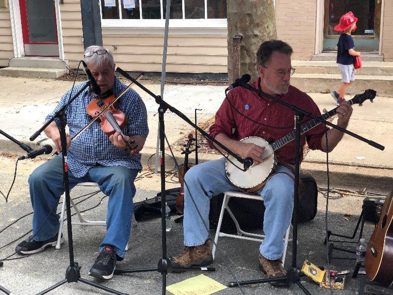 Two musicians play a fiddle and a banjo on the street at the Friendship Festival.